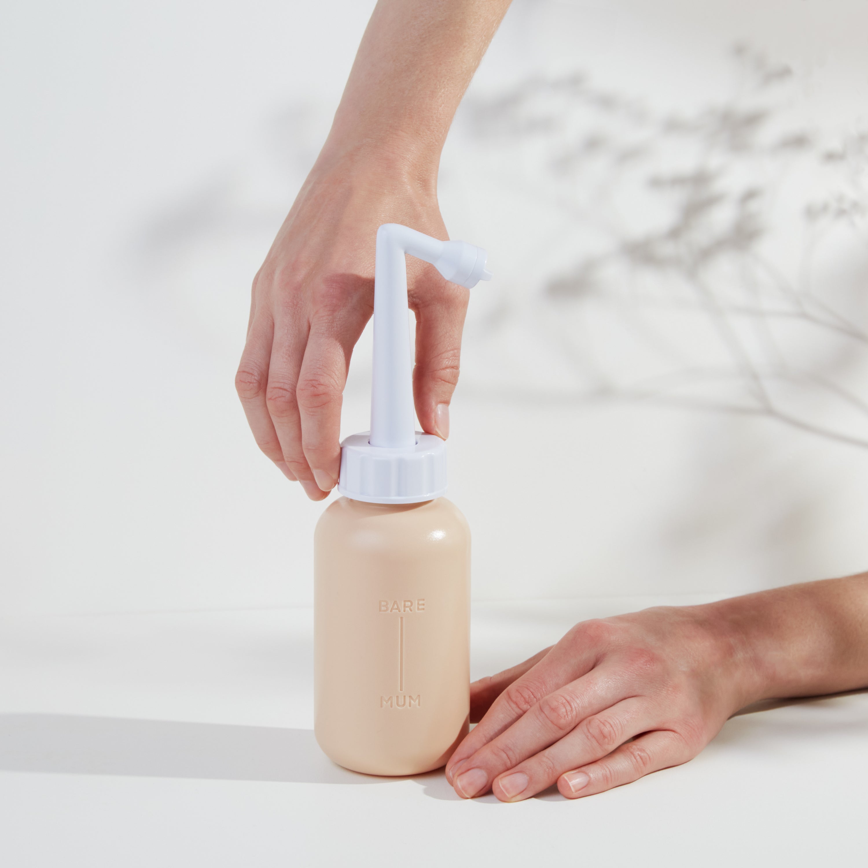 two hands holding bare mum perineal wash bottle in a way that suggests they are unscrewing the top from the base