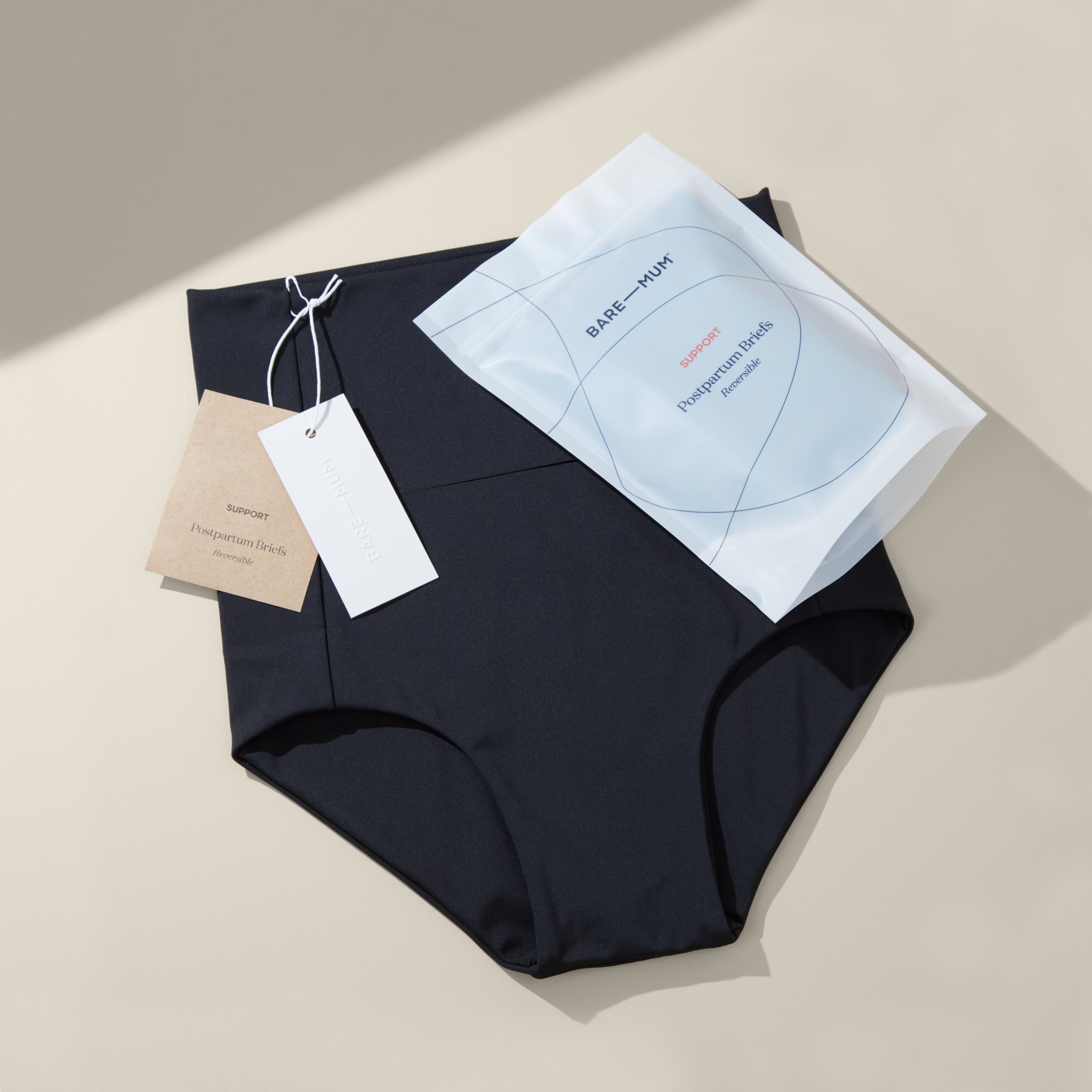 Pair of bare mum postpartum briefs laid flat on neutral background , shows tags and packaging laying on top